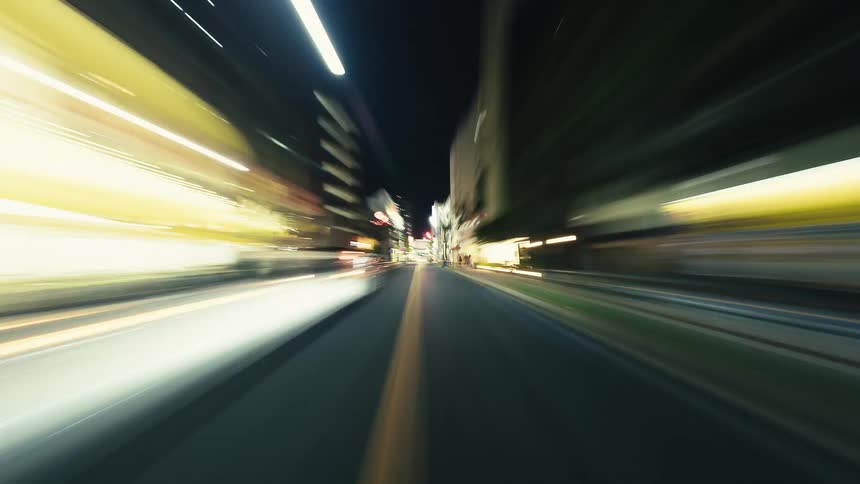 A high-speed hyper-lapse drive through a brightly lit city at night, with light trails creating a sense of motion