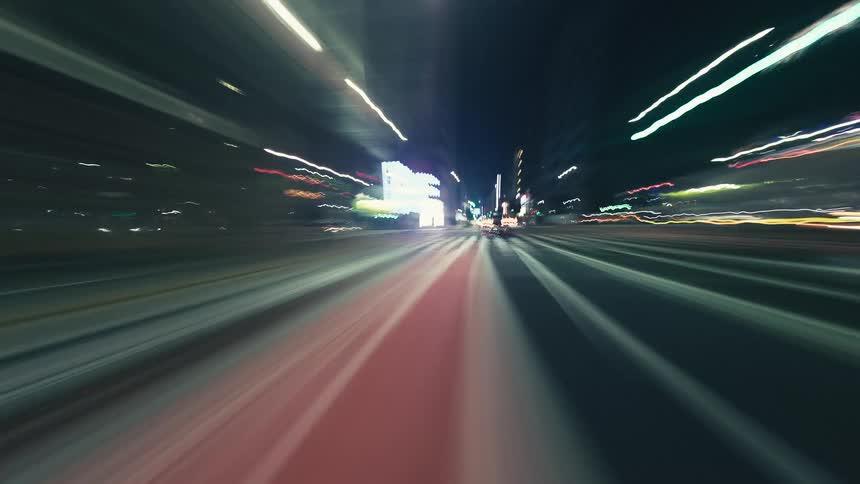 Dynamic nighttime hyperlapse POV driving through city streets, creating a blur of vibrant light trails
