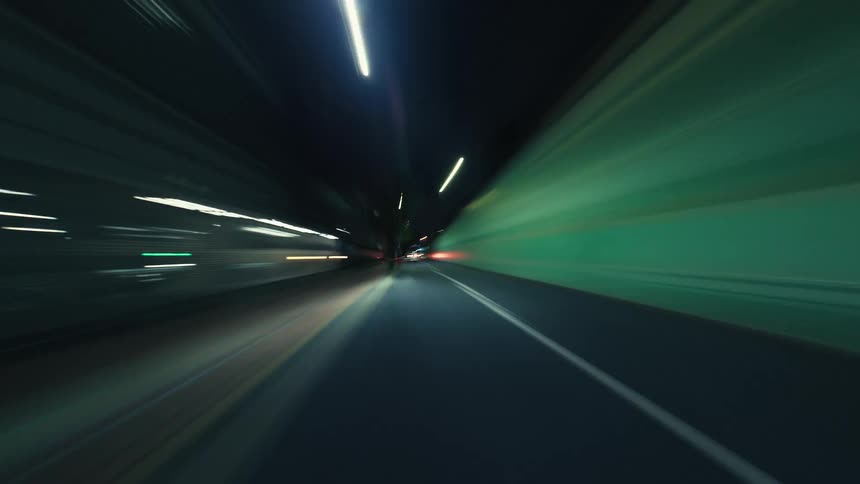 A futuristic hyperlapse POV of driving at high speed through a city at night, creating vibrant streaks of light from traffic and buildings