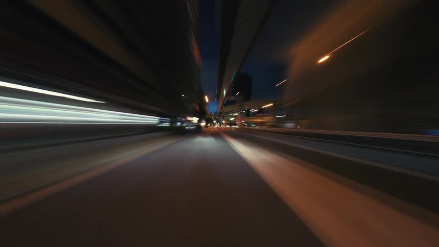 A first-person view hyperlapse captures a high-speed drive through a modern city at night, with light trails creating a blur of motion