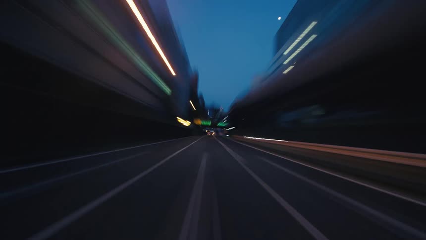 A driver's point-of-view hyperlapse speeds along a city highway at twilight, creating mesmerizing light trails from buildings and traffic