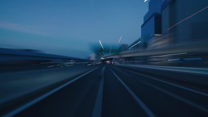 Point-of-view hyperlapse drive on a modern city highway at dusk, surrounded by towering skyscrapers and mesmerizing light trails