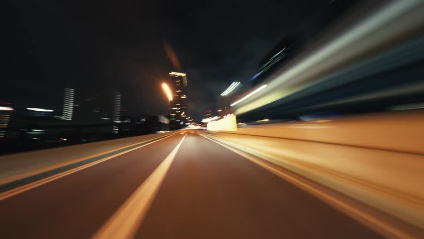 Point-of-view time-lapse of a high-speed drive through a modern city at night, with blurred lights creating vibrant streaks
