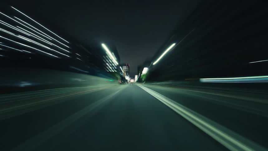 A dizzying point-of-view hyperlapse of driving through city streets at night, creating vibrant light trails