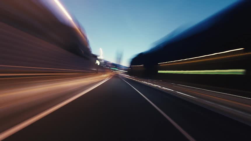 A high-speed point-of-view hyperlapse shows glowing light trails while driving through a modern city at night