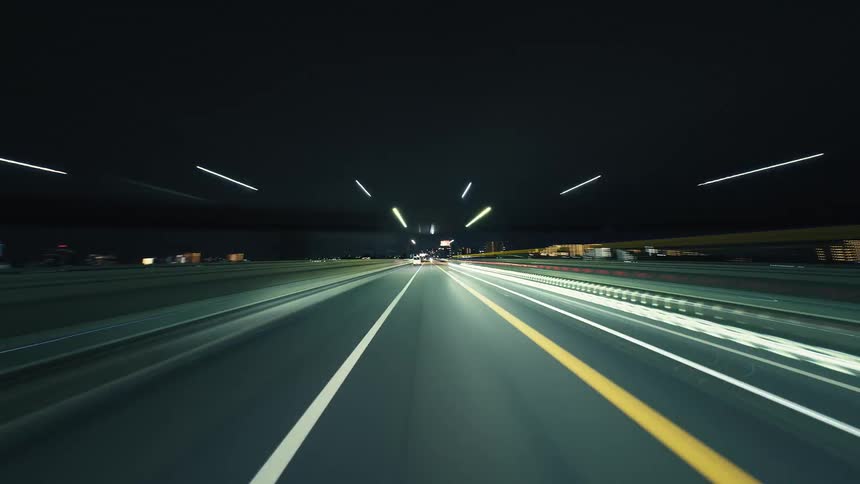 A dynamic POV hyper-lapse captures a high-speed drive along a city expressway at night, with light trails creating a futuristic and energetic scene
