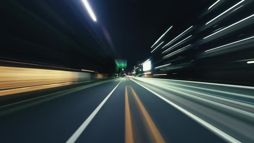 A dynamic POV hyperlapse of a car speeding through city streets at night, capturing the motion blur of urban lights