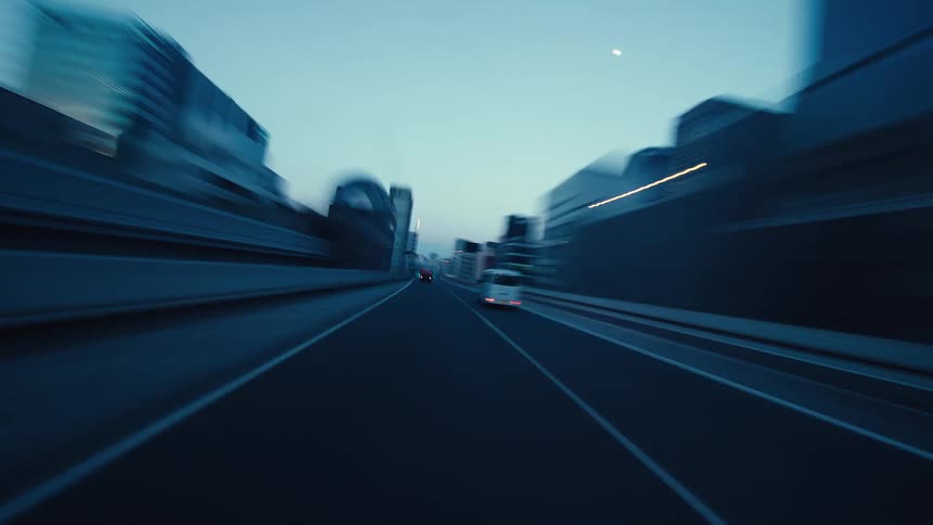 A futuristic, low-angle time-lapse captures a high-speed drive through a city highway at dusk, with light trails creating a sense of motion and energy
