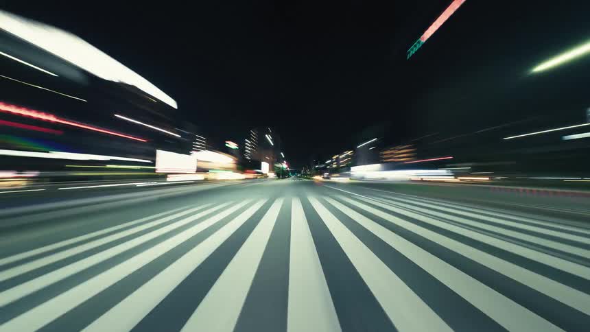 A fast-paced hyperlapse from a driver's point of view captures the vibrant light trails of a modern city at night