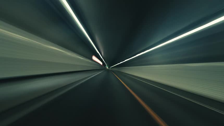 A futuristic POV timelapse captures a high-speed drive along a city highway and through tunnels at dusk, with light trails blurring into streaks of motion