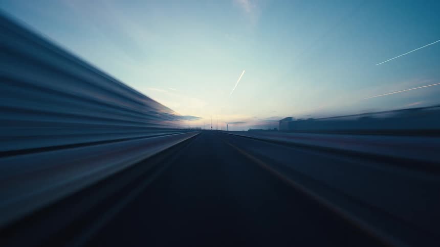 A fast-paced hyper-lapse from a driver's perspective on a city highway at dusk, with light trails streaking across the screen