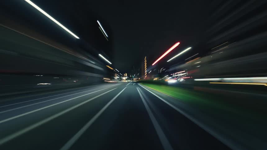 A dynamic first-person point-of-view hyperlapse shows the dazzling blur of city lights while speeding through urban streets at night