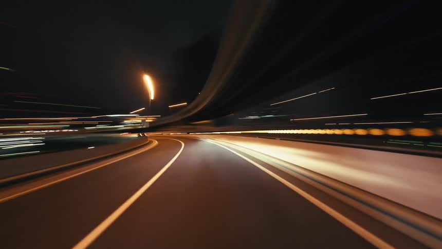 A futuristic point-of-view hyperlapse of a high-speed drive through a city at night, with colorful light trails streaking across the screen