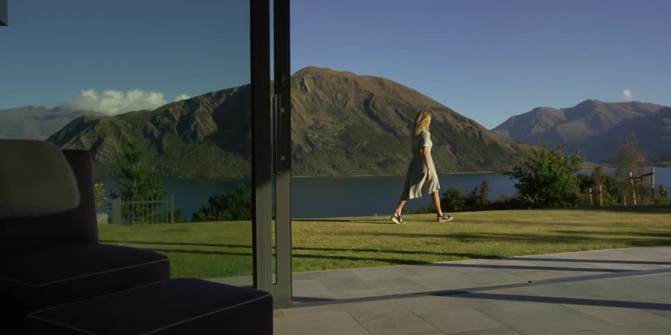 A woman walks on a lawn overlooking a mountain lake