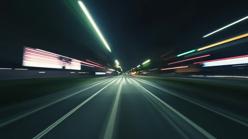 A fast-paced hyperlapse from a car driving through the city at night, with streetlights blurring into streaks of color