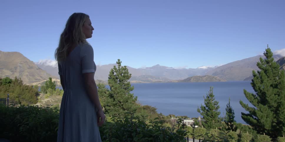 Woman looks out at a lake surrounded by trees and mountains