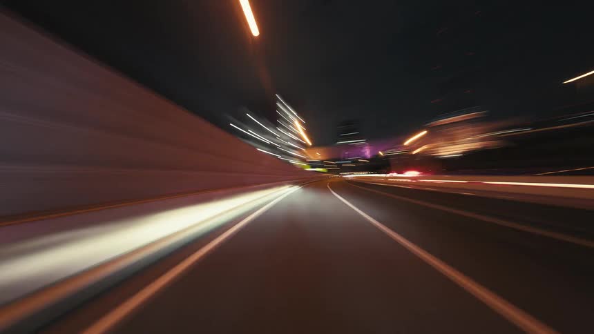 A mesmerizing point-of-view timelapse captures the blur of city lights while driving at high speed down a highway at night