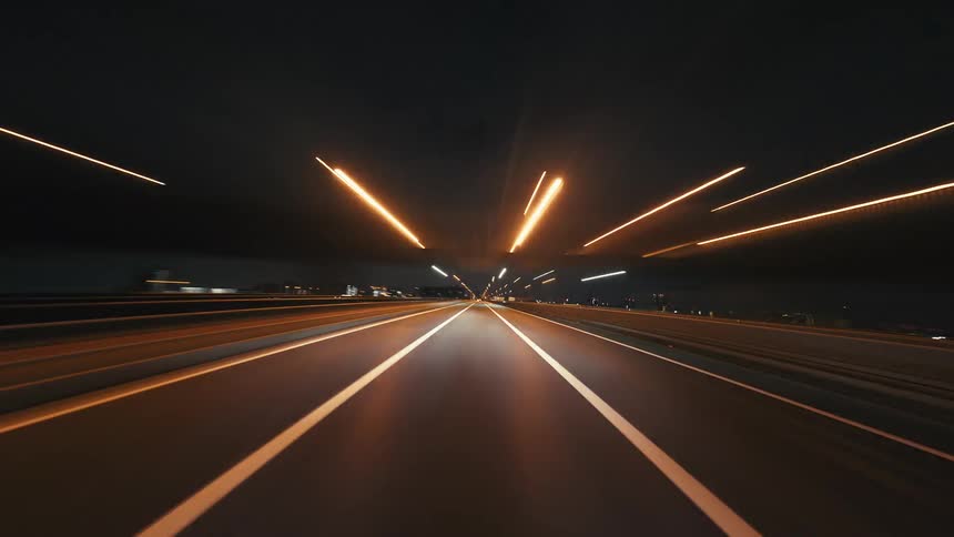 A fast-paced POV hyperlapse of driving on a city highway at night, with streetlights and traffic creating dynamic light streaks