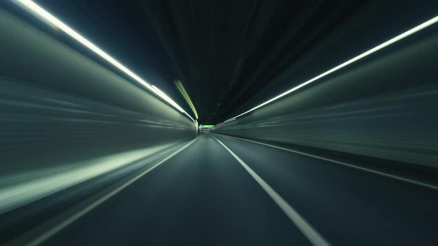 A futuristic POV timelapse shows a high-speed drive through a city at night, with vibrant light trails illuminating the tunnels and highways