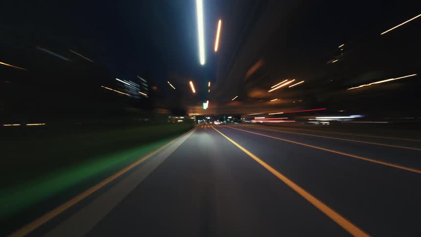 A high-speed time-lapse from a car's perspective driving through a city at night, with vibrant light trails streaking across the screen