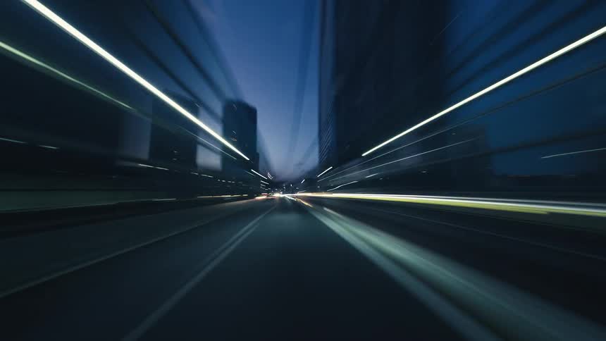 A futuristic point-of-view hyperlapse shows a vehicle speeding down an empty city highway at night, creating mesmerizing light trails