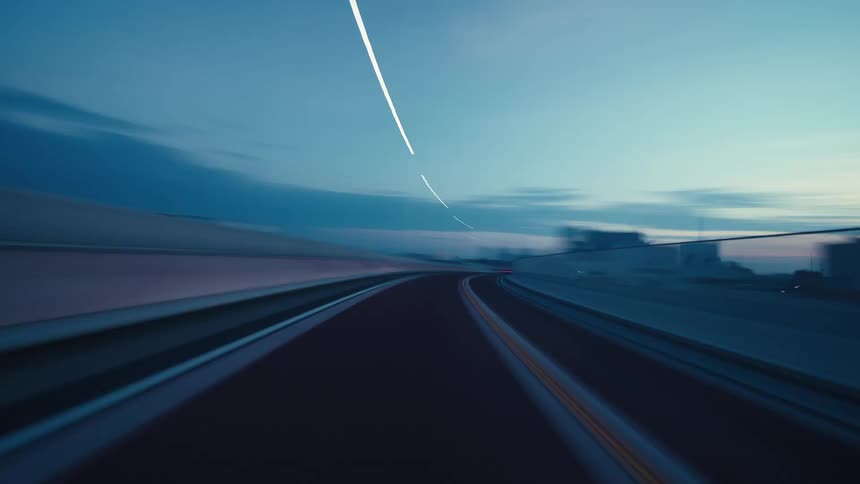 Cinematic POV time-lapse captures a high-speed drive through a modern city at twilight, with blurred surroundings and streaks of light