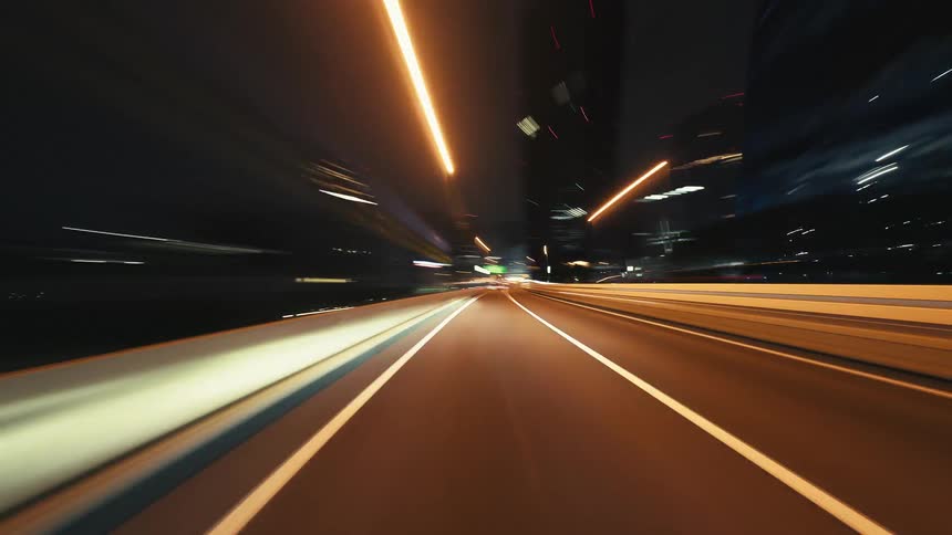 A seamless POV time-lapse of a fast night drive on a city highway, with urban lights blurring into long, colorful streaks