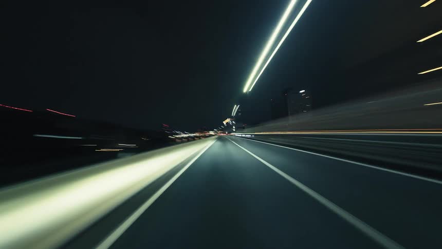 A thrilling point-of-view hyperlapse of driving on a city highway at night, with traffic and streetlights creating vibrant light trails