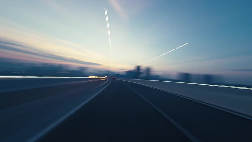 Point-of-view hyperlapse of a fast drive over a modern suspension bridge towards a city skyline at twilight