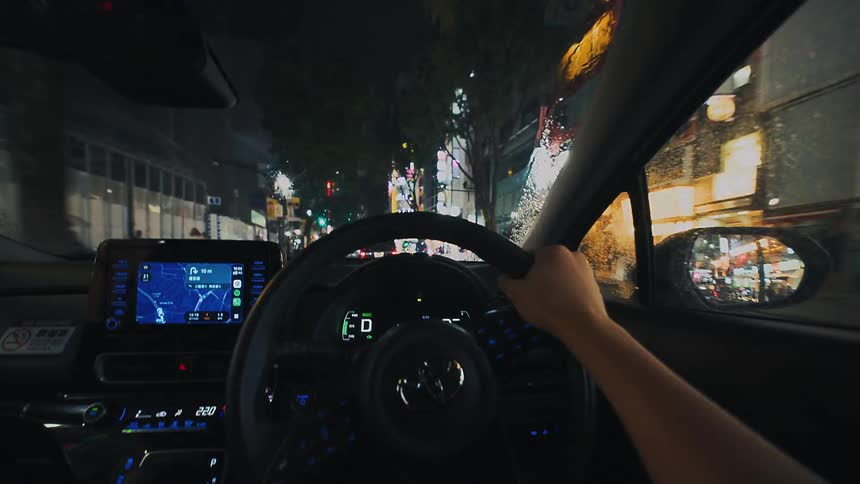 Point-of-view of driving through the bright, neon-lit streets of a city at night during a rainstorm