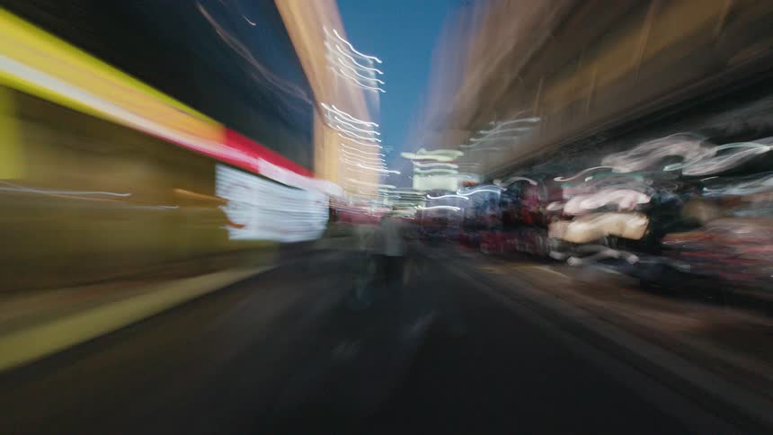 A dizzying first-person hyperlapse captures the energetic nightlife of a bustling city street with intense motion blur and vibrant light streaks