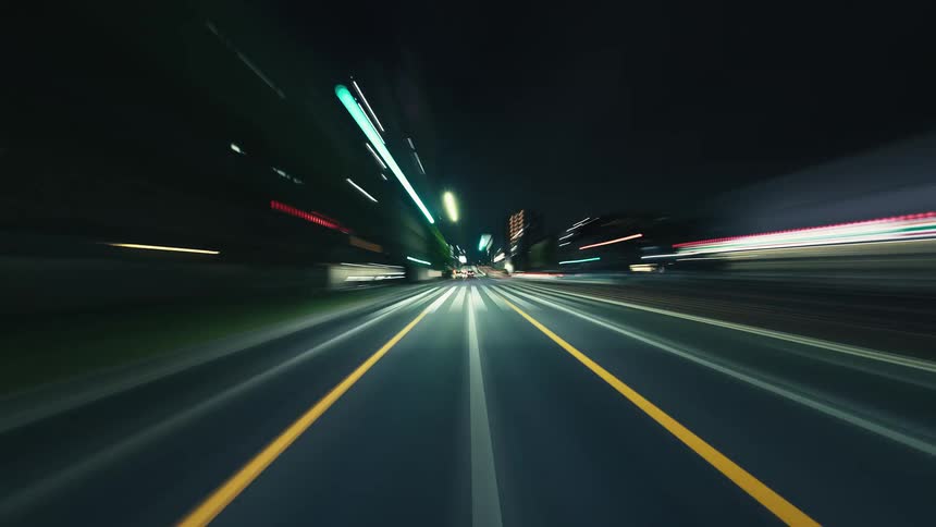 A high-speed hyperlapse from a driver's perspective captures the vibrant, blurred light trails of a city at night
