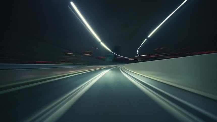 A point-of-view hyperlapse shows a car speeding down an empty highway at night, with city lights and streetlights blurring into long streaks