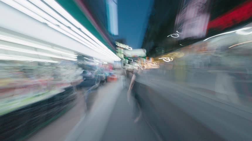 A dizzying first-person hyperlapse speeds through a bustling city market street at night, with lights blurring into streaks of color