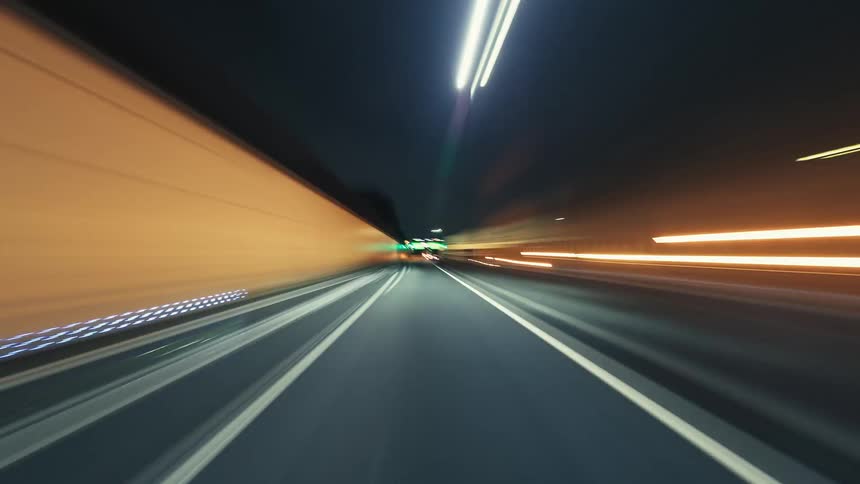 A futuristic POV time-lapse of a high-speed drive through a city highway and tunnels at night, with vibrant light trails blurring past