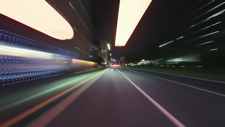 A futuristic POV hyperlapse shows a car speeding through a city at night, turning the urban landscape into a vibrant blur of colorful light trails