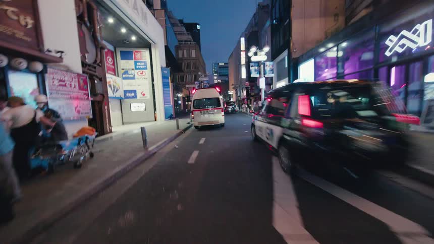 A high-speed, first-person hyperlapse navigates the vibrant, neon-lit backstreets of a bustling Japanese city at night