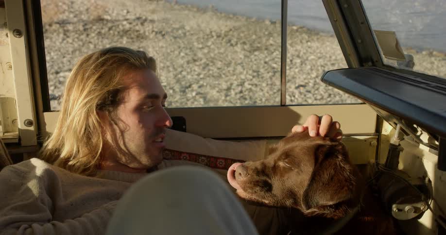 A man pets a dog while laying inside a vehicle