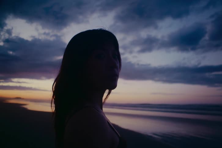 Close up of a woman's silhouette as she contemplates the ocean during a beautiful, cloudy sunset