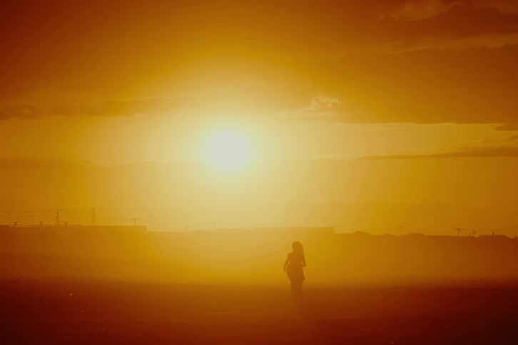 A solitary woman runs through a vast, hazy landscape bathed in the intense orange light of the setting sun