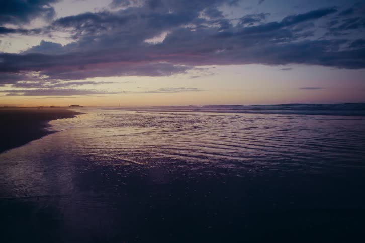 Calm ocean waves gently wash ashore on a tranquil beach under a moody purple sky at twilight