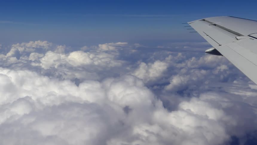 POV from an airplane passenger window soaring over a thick blanket of white clouds on a sunny day