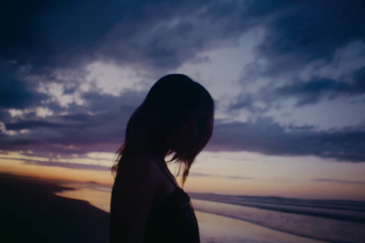 The silhouette of a woman standing on the shore at dusk, contemplating the ocean under a cloudy sky