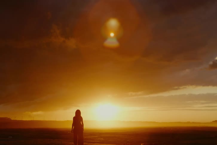 In slow motion, the silhouette of a woman walks toward a dramatic golden sunset