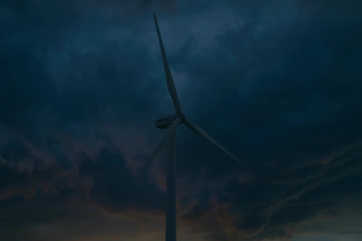 A single wind turbine spins slowly, silhouetted against a dark and stormy sky at dusk