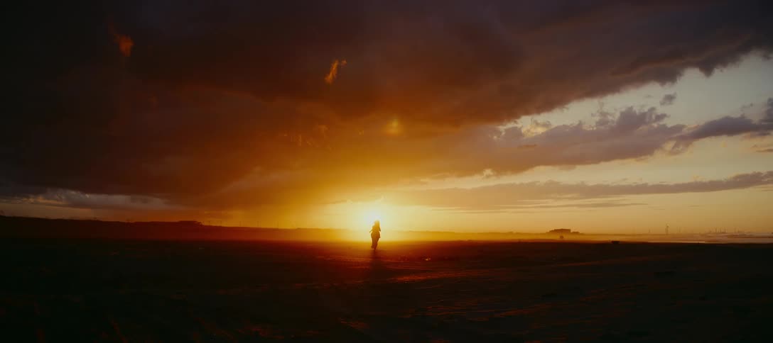 A silhouetted woman runs in slow motion across a vast landscape towards a dramatic and fiery sunset