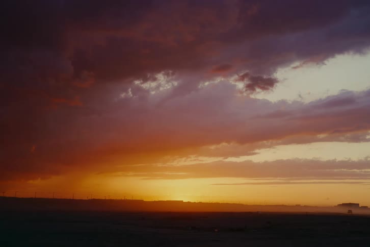 A dramatic and colorful sunset with orange and purple clouds hangs over a silhouetted landscape