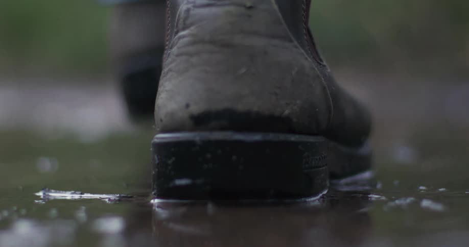 Super slow motion close up of a heavy leather boot splashing into a muddy puddle and then lifting out