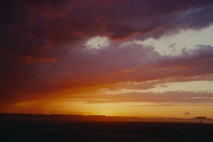 Dramatic fiery orange and purple sunset with dark clouds over a desolate landscape as a single bird flies by