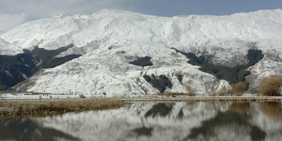 The snow covered mountain has a calm lake in front